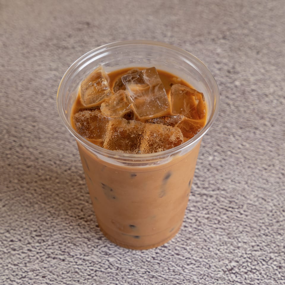 Clear plastic cup filled with iced coffee sits on a speckled countertop.