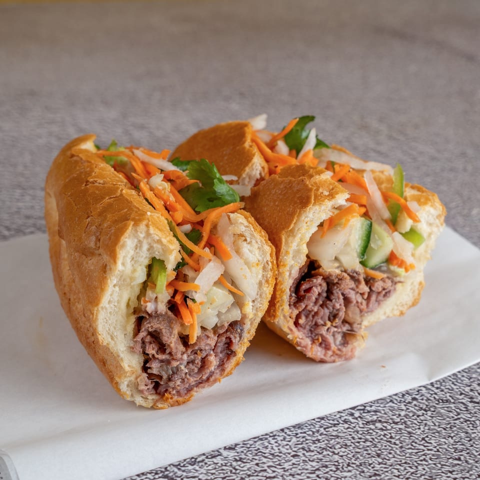Pho dip banh mi with braised beef, pickled carrots, daikon, and cilantro on a crusty roll.